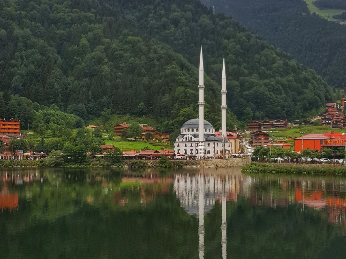 Still water of Uzungöl reflecting the forested mountainside and the lakeside mosque
